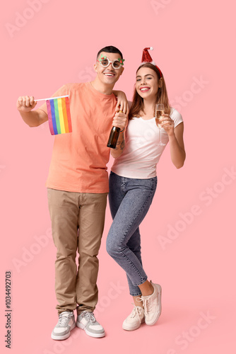 Young couple with LGBT flag and champagne on pink background