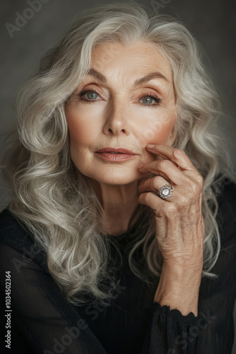 An elegant elderly Caucasian woman showcases her beauty with wavy hair and delicate rings on her fingers. Her makeup enhances her features beautifully, with a soft background that reflects her grace