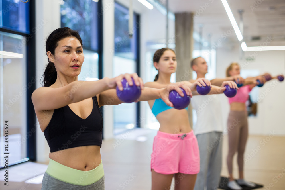 Obraz premium Focused active young adult woman doing workout with toning weight balls at group pilates class