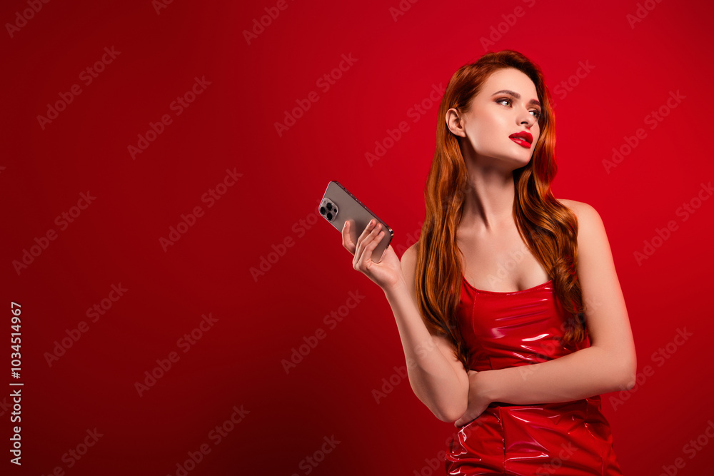 Naklejka premium Photo of attractive woman look empty space hold device dressed sexy leather clothes isolated on red color background