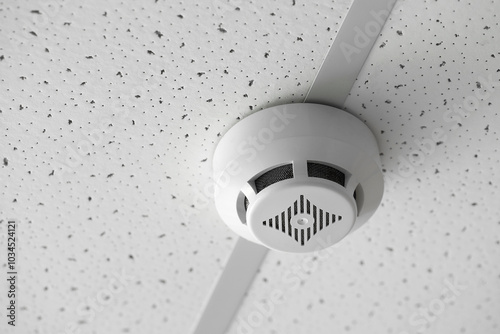 Modern smoke detector on ceiling in room, closeup photo