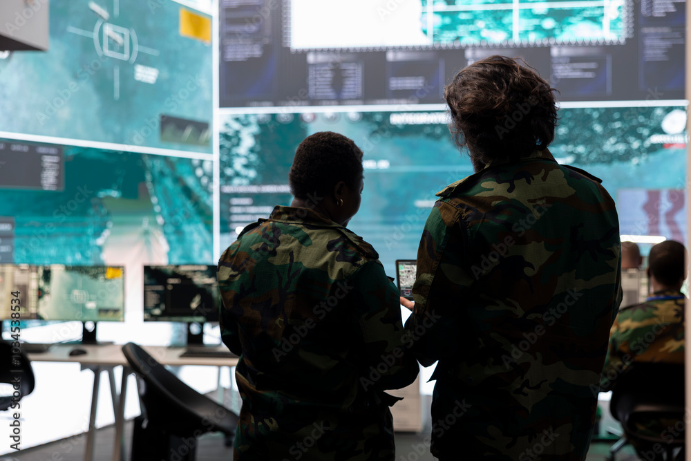 Fototapeta premium Diverse team of military personnel analyzing battlefield real time data on CCTV radar satellite system, transmitting information to soldiers in the field. Army superiors work on defense program.