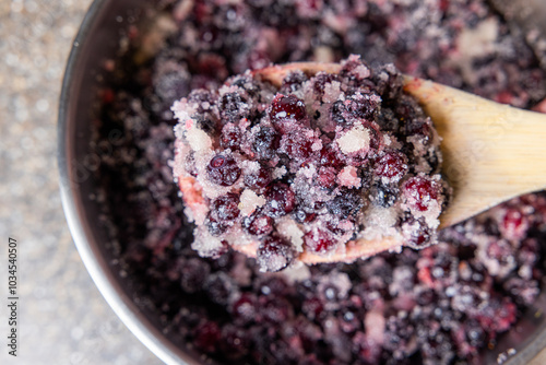 A bowl of berries with sugar and in a pot. The bowl is silver and the berries are wild huckleberries. photo