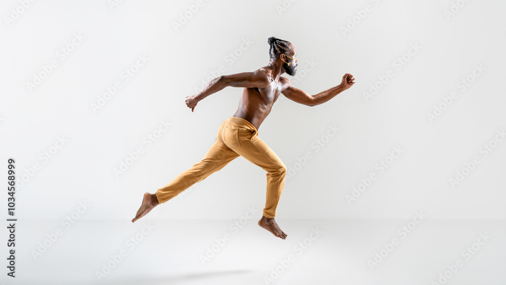 Fototapeta premium Determined shirtless gay model jumping over gray background. Full body side view of strong young man is in midair at plain studio.