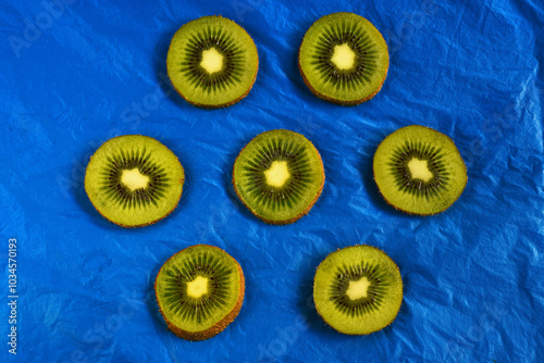 Top down view of seven kiwi slices in a pattern on dark blue background.