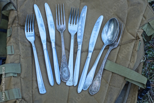 set of gray metal spoons forks and table knives lie on brown fabric backpack on summer street