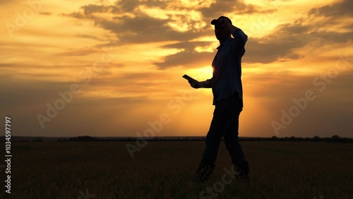 Worker walks in rubber boots at sunset. Agricultural business. Farmer works in rubber boots, field with young green sprouts. Businessman grows food. Grow grain, vegetables. Field, young green shoots