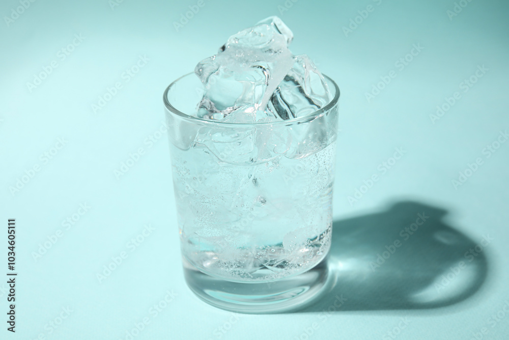 Refreshing water with ice in glass on turquoise background, closeup Refreshing water with ice in glass on turquoise background, closeup