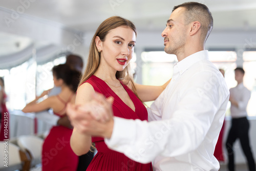 Elegant stylish woman in red dress enjoying slow foxtrot with male partner in dance studio. Amateur ballroom dancing concept.. photo