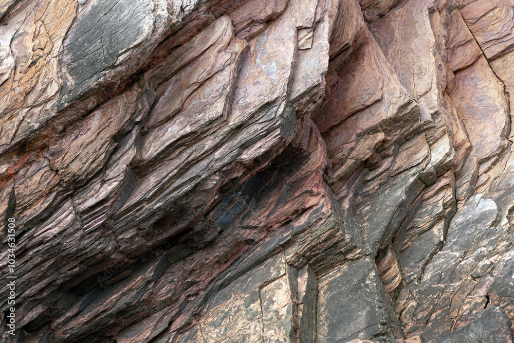 Close-up view of stratified rock formations, featuring layers of various shades of brown, reddish, and grey tones. The rugged texture and visible cracks highlight the natural geological processes Close-up view of stratified rock formations, featuring layers of various shades of brown, reddish, and grey tones. The rugged texture and visible cracks highlight the natural geological processes