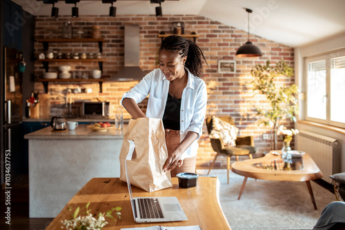 Young woman opening her food delivery bag at home in the kitchen