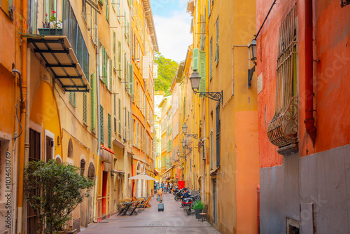 Fototapeta Naklejka Na Ścianę i Meble -  A tourist pulls her suitcase along a narrow alley in the colorful Vieux Nice Old town of Nice, France, on the French Riviera, Cote d'Azur of the Mediterranean Sea.