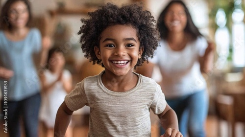 A young child with curly hair smiles brightly as they run energetically towards the viewer, surrounded by happy family members enjoying playful moments in the background of a cozy room.