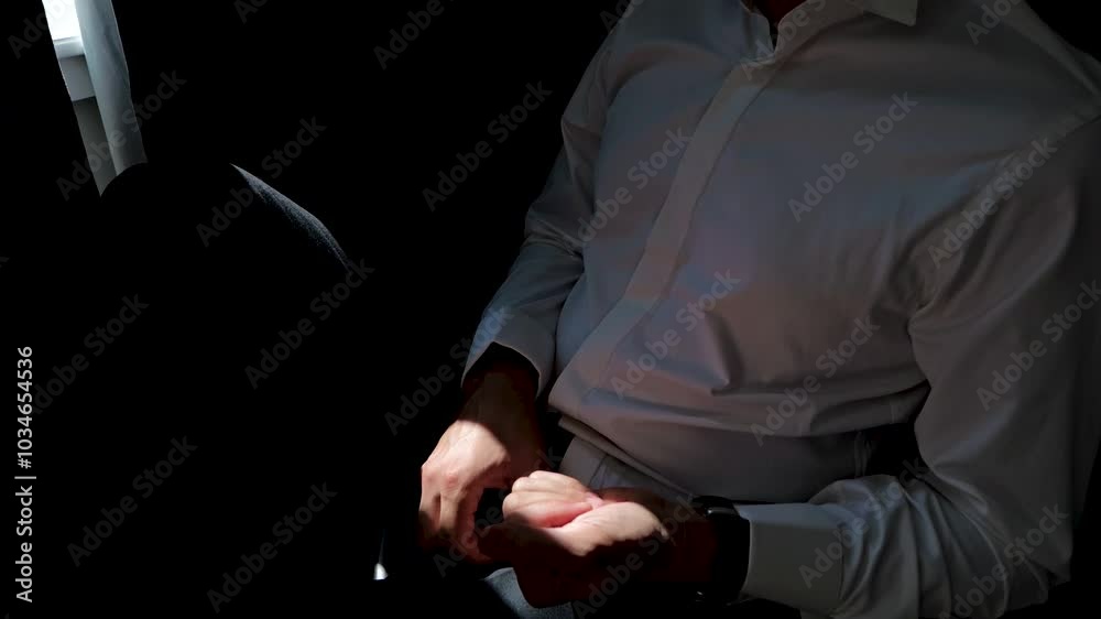 The man sits on a chair around the window and holds two rings in his hand. The man sits on a chair around the window and holds two rings in his hand.