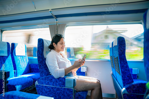 A happy young Latina woman, seated comfortably on a high-speed train in Japan, smiles while using her smartphone, enjoying the scenic views during her fast-paced journey.
