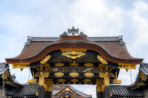 A close-up view of the beautifully ornate entrance gate at Nijo Castle in Kyoto, Japan. The gate features intricate gold details and traditional Japanese architectural designs, showcasing the castle's photo