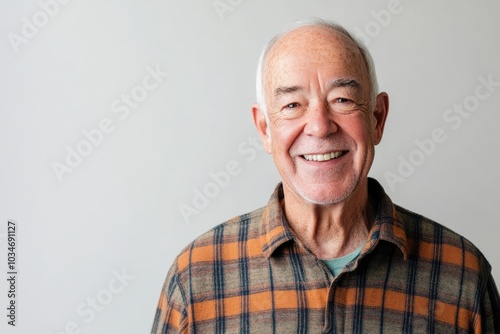 Elderly man, smiling broadly, standing against a solid light gray background with room for messaging