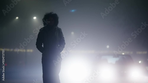 Mysterious woman walking in fog at night backlit by car traffic headlights