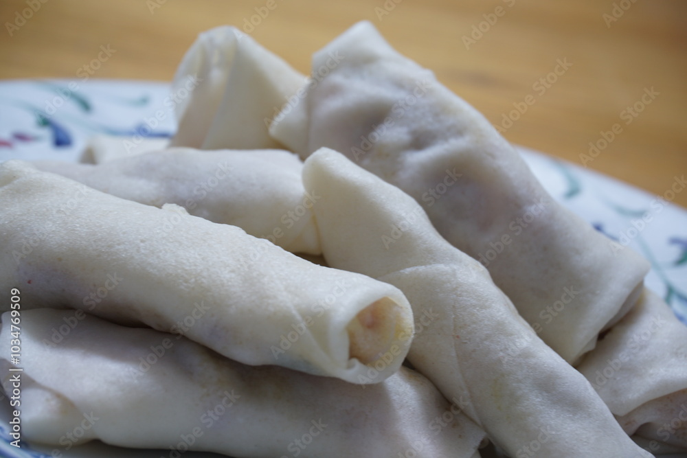 Heap of raw spring rolls(lumpia) on the plate. Frozen food on wooden tables. Heap of raw spring rolls(lumpia) on the plate. Frozen food on wooden tables.