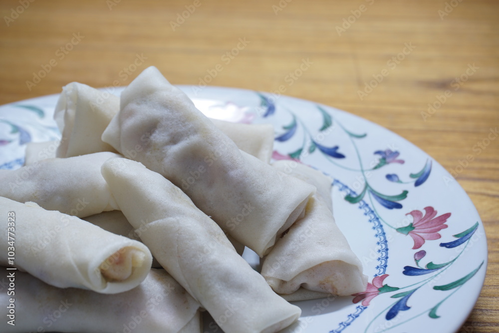 Heap of raw spring rolls(lumpia) on the plate. Frozen food on wooden tables. Heap of raw spring rolls(lumpia) on the plate. Frozen food on wooden tables.