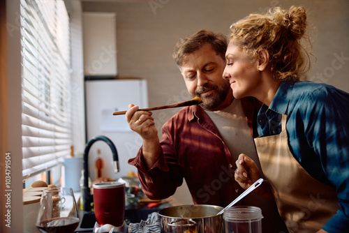 Smiling couple tasting food while preparing Thanksgiving dinner and cooking in kitchen. photo