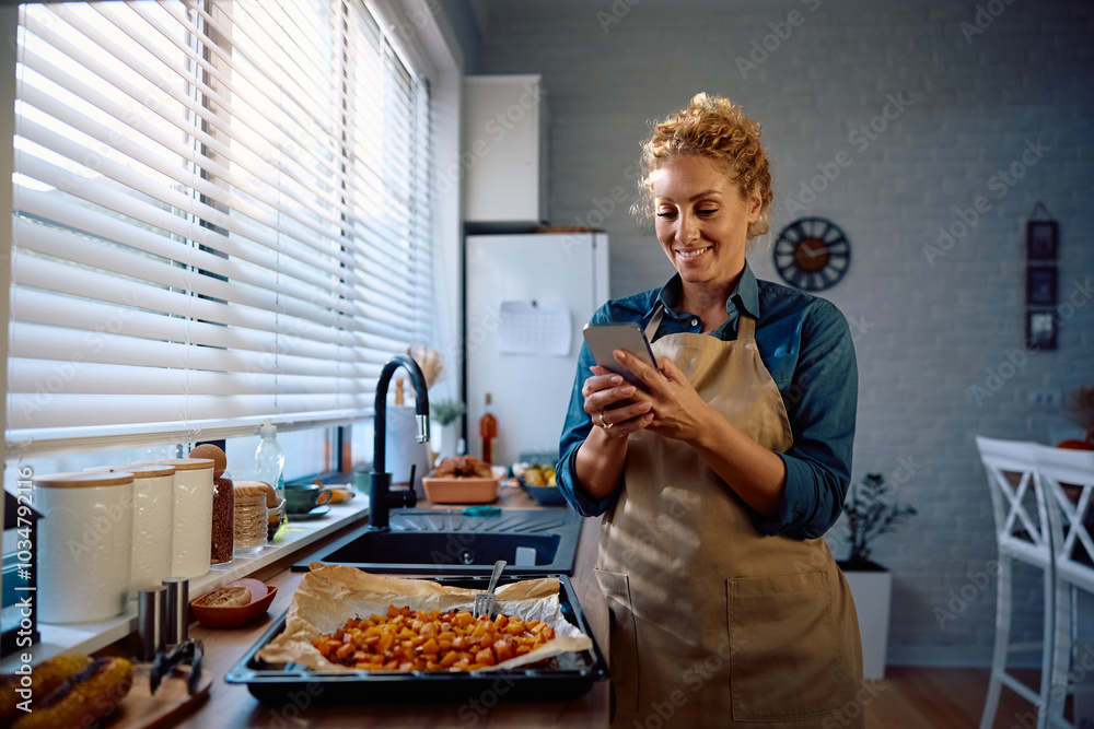 Happy woman texting on cell phone while preparing Thanksgiving meal in kitchen. Happy woman texting on cell phone while preparing Thanksgiving meal in kitchen.