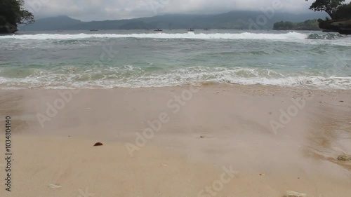 Tropical beach view and crashing waves with brownish white sand and blue sea