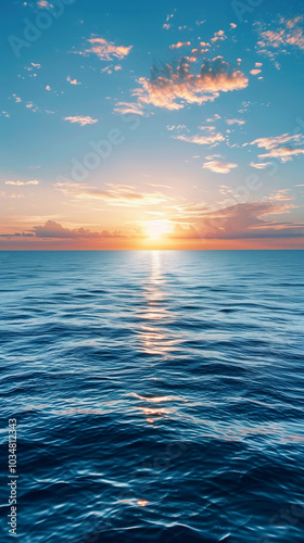 The tranquil sea stretches endlessly, reflecting the vibrant colors of the sunset. Soft clouds drift above as the horizon meets the glowing sun, creating a peaceful atmosphere