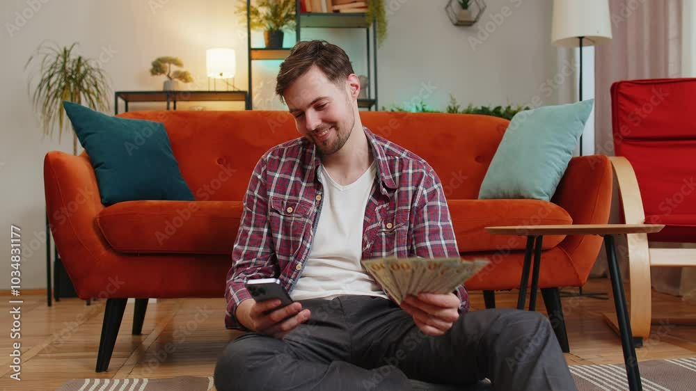 Successful rich man holding smartphone and waving dollar bill money fan sitting in living room at home. Happy Caucasian guy winning online lottery game planning vacation calculating budget concept Successful rich man holding smartphone and waving dollar bill money fan sitting in living room at home. Happy Caucasian guy winning online lottery game planning vacation calculating budget concept