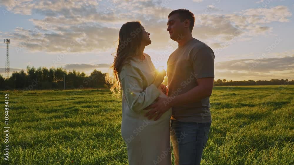 Expecting parents embrace in a sunset field during a pregnancy celebration Expecting parents embrace in a sunset field during a pregnancy celebration