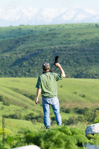 A man is standing in a grassy field with a camera in his hand photo