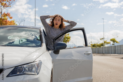 Stressed young woman stranded in the middle of the road because her car broke down. She calls for help on her phone, waiting for the tow truck. Roadside assistance. Reflective vest and triangle.