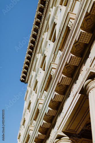 Elegant Neoclassical Facade with Ornate Columns and Intricate Cornices - Low-angle view of neoclassical architecture with detailed columns and ornate cornices against a clear blue sky