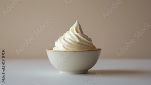 A bowl of delicate whipped cream rests on a pristine surface, highlighting its creamy consistency and soft texture.