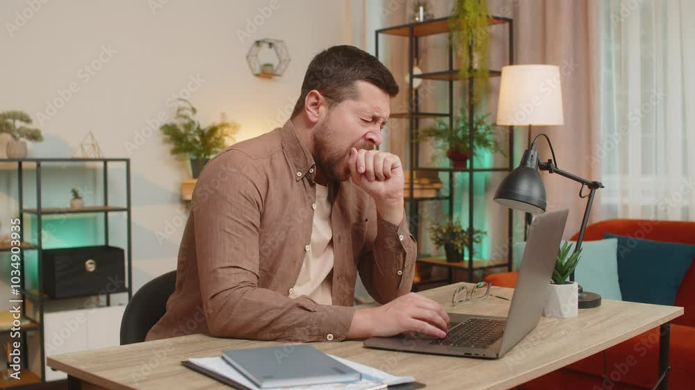 Bored sleepy young businessman working on laptop yawns, sleeping on netbook at home office desk in living room. Exhausted tired Caucasian freelancer workaholic man. Employment, occupation, workless.