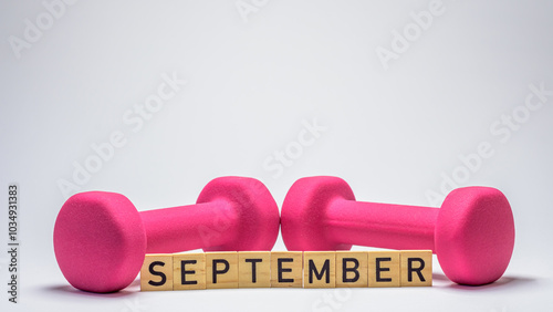 wooden blocks spelling 'September' in front of a pink dumbbells on a white background. This minimalist composition symbolizes fitness goals, motivation, and a fresh start.	