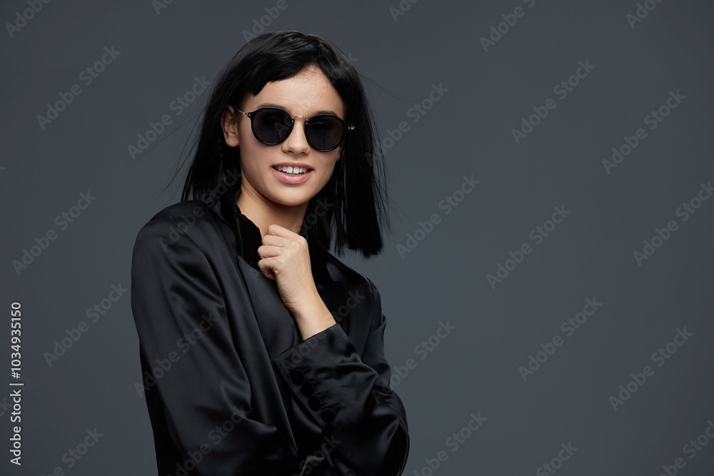 Woman in sunglasses and black shirt, smiling with hands on hips, posing against a gray background Woman in sunglasses and black shirt, smiling with hands on hips, posing against a gray background