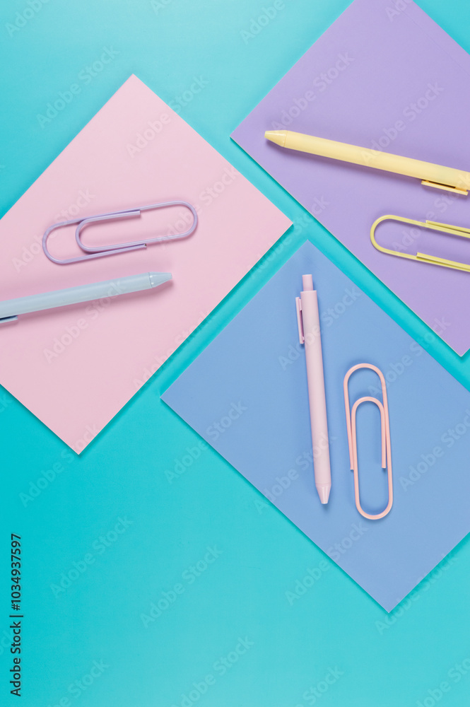 Top view of pink, purple and blue notebooks on blue background. Pink, yellow and blue pens, paperclips, school, office wallpaper. Flat lay, copy space. Top view of pink, purple and blue notebooks on blue background. Pink, yellow and blue pens, paperclips, school, office wallpaper. Flat lay, copy space.