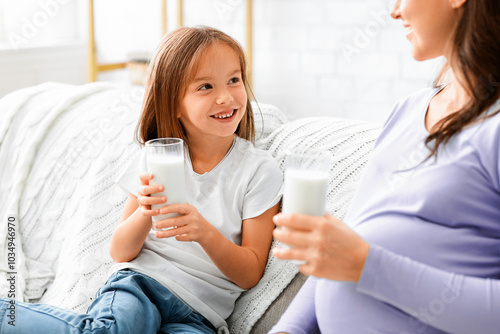 Close up of preschooler happy girl enjoying milk with her pregnant mom, nutririon and healthy lifestyle concept photo