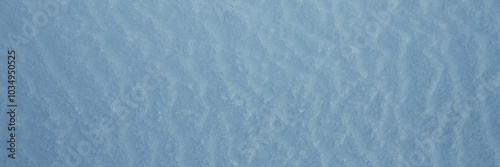 Beautiful winter background with snowy ground. Natural snow texture. Wind sculpted patterns on snow surface. Wide panoramic texture for background and design. Closeup top view with copy space.