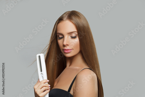 Attractive fashion model woman using hair straighteners iron on white background. Harstyle, hair care, beauty salon and treatment concept