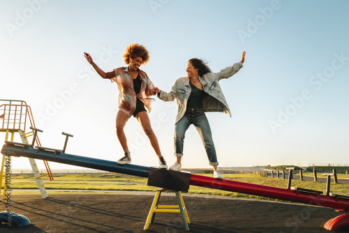 High school friends balancing on a seesaw in a sunny park, enjoying a fun moment together