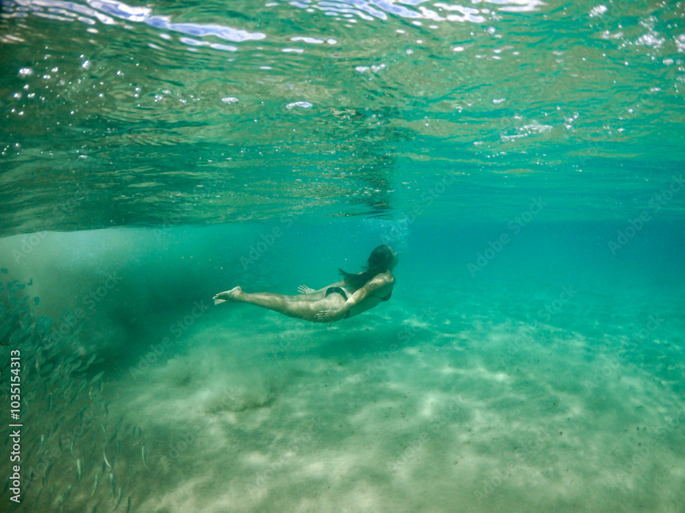 Naklejka premium Underwater view of a woman swimming with a school of fish in Fernando de Noronha, Brazil