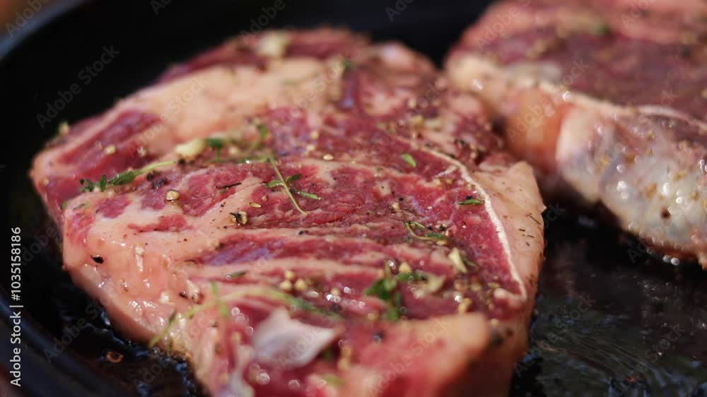 Two juicy rib-eye steaks are seasoned with salt, pepper, and thyme, and seared on a hot pan. Close-up of the cooking process. Two juicy rib-eye steaks are seasoned with salt, pepper, and thyme, and seared on a hot pan. Close-up of the cooking process.