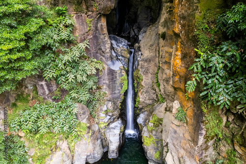 Aerial view of cascata do salto waterfall surrounded by lush green vegetation and rocky cliff formations, Ribeira Grande, Portugal. photo