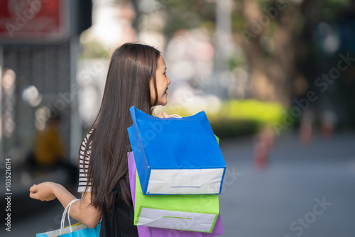 Happy Asian woman in modern dress holding shopping bags walking outside shopping mall