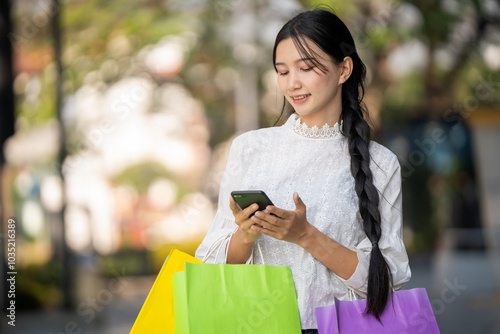 Asian woman in modern dress holding shopping bags walking outside a shopping mall.