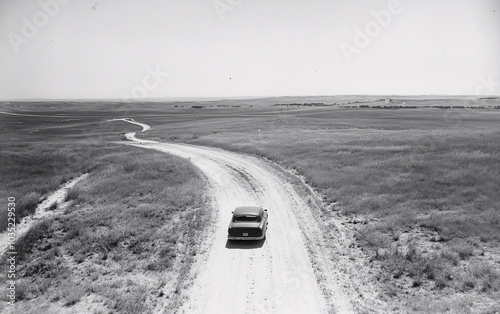 Aerial view of a car driving through a vast open landscape in a vintage film style, capturing the sense of isolation, freedom, and adventure on a remote countryside road.