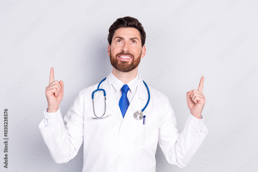 Portrait of experienced doctor man look indicate fingers up empty space wear white coat isolated on grey color background Portrait of experienced doctor man look indicate fingers up empty space wear white coat isolated on grey color background