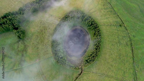 Aerial view of tranquil Lagoa Pau Pique surrounded by lush green forest and clouds, Capelas, Portugal. photo